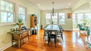 A spacious dining area with a long wooden table, surrounded by chairs, and large windows offering views of the outdoors. - Otium Villa - Waterfront, intercoastal villa with a Spa-like feel. (Port Orange)