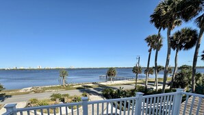 A deck with white railings overlooking a body of water, palm trees, and a distant city skyline. - Otium Villa - Waterfront, intercoastal villa with a Spa-like feel. (Port Orange)
