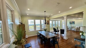A spacious dining area with a wooden table and chairs, large windows with a view, and a cozy living room with a sofa and a lamp. - Otium Villa - Waterfront, intercoastal villa with a Spa-like feel. (Port Orange)