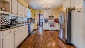 A kitchen with wooden flooring, white cabinets, a stainless steel refrigerator, and a tiled backsplash. - Cozy Craftsman in the Center of Oak Cliff (Dallas)