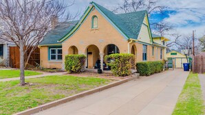 A two-story house with a green roof, a front porch, and a small front yard. - Cozy Craftsman in the Center of Oak Cliff (Dallas)