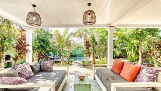 A covered outdoor seating area with two sofas, a coffee table, and a view of a pool and lush greenery.