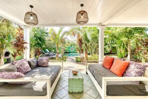 A covered outdoor seating area with two sofas, a coffee table, and a view of a pool and lush greenery.