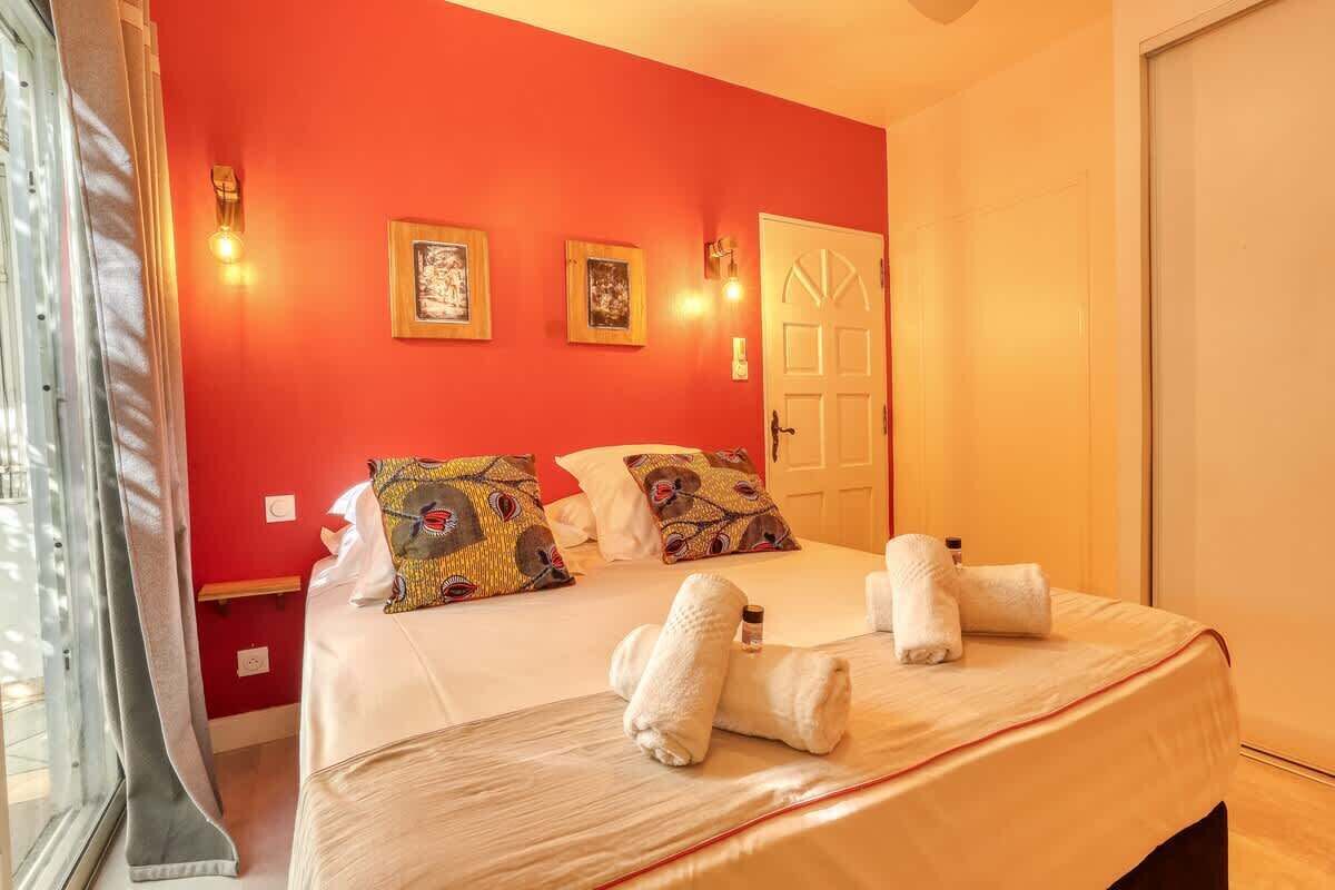 Ein Hotelzimmer mit roter Wand, einem Bett mit weißer Bettwäsche, zwei gerahmten Bildern und einer Tür.