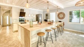 A modern kitchen with a large island, bar stools, pendant lighting, and a view of the outdoors.