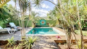 A pool surrounded by tropical plants and a wooden deck with lounge chairs.