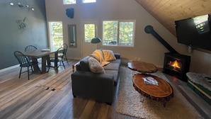 Un acogedor salón tipo loft con chimenea, pisos de madera y ventanas amplias.
