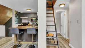 Una cocina moderna con techo de madera, una isla central con taburetes de bar y una escalera con detalles de madera.