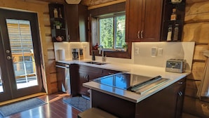 A modern kitchen with a central island, wooden cabinets, a window, and a built-in toaster. - Bear Behind Lodge (Fraser Valley C)