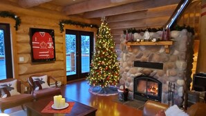 A cozy log cabin interior with a stone fireplace, a Christmas tree, and festive decorations. - Bear Behind Lodge (Fraser Valley C)