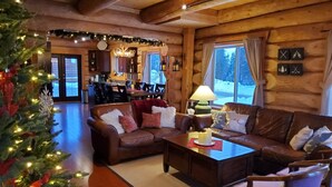 A cozy log cabin interior with a fireplace, a dining area, and a Christmas tree. - Bear Behind Lodge (Fraser Valley C)
