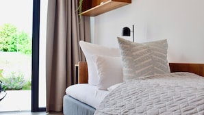 A modern bedroom with a bed, a wooden shelf above it, and a view of greenery outside. - TIN INN Montabaur (Montabaur)