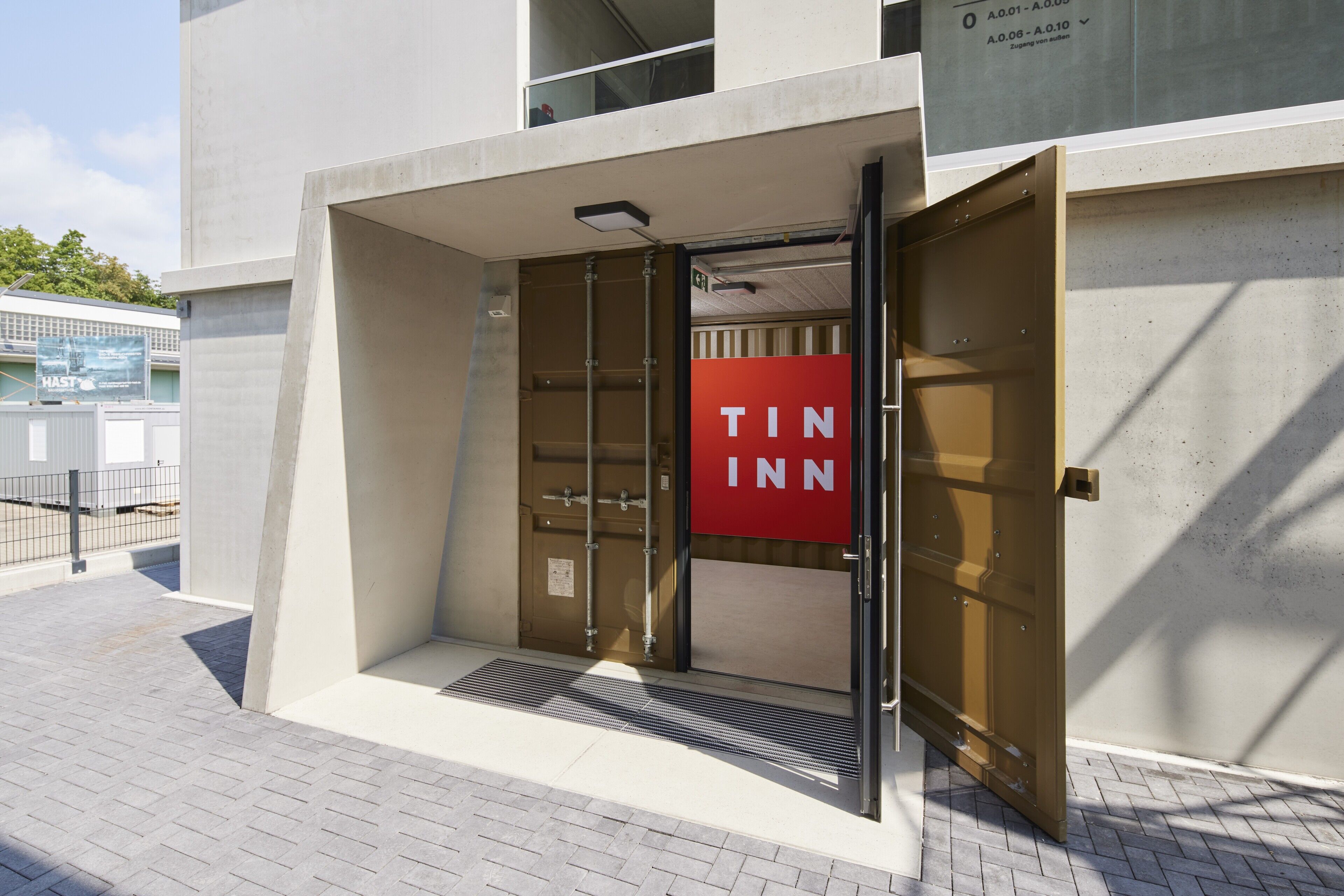 Una entrada moderna de edificio con un letrero rojo que dice "TIN INN" y una puerta de metal.