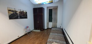 Ein kleiner Raum mit einem Bett, einem Sessel, einem Schrank und einem Bild an der Wand.