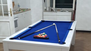 Une table de billard avec des billes et des queues, un meuble blanc avec une fenêtre et un plancher en bois.