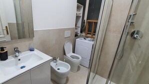 Une salle de bain compacte comprenant un lavabo, un bidet, des toilettes et une douche à parois de verre.