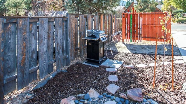 A backyard with a wooden fence, a barbecue grill, and a small shed. - Bill Big Bear Bunkhouse (Big Bear City)