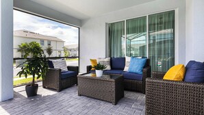 Een balkon met rieten meubels, een bloempot en uitzicht op omliggende gebouwen.