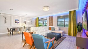 Ein modernes Wohnzimmer mit einem weißen Sofa, bunten Stühlen, einem Esstisch und Kunstwerken an den Wänden.