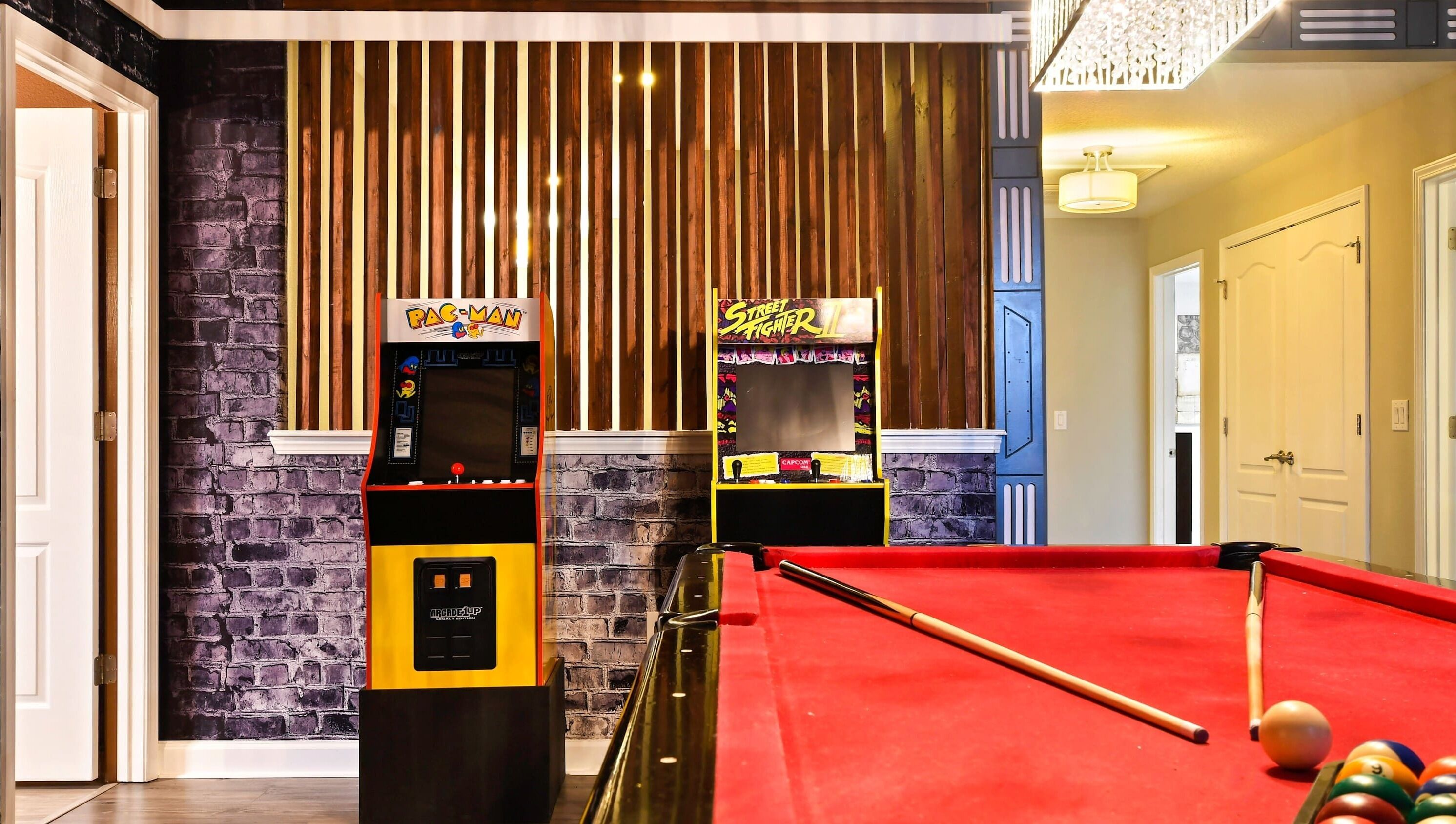 A pool table with a red felt surface, two arcade machines labeled 'Pac-Man' and 'Street Fighter II', and a brick-patterned wall.