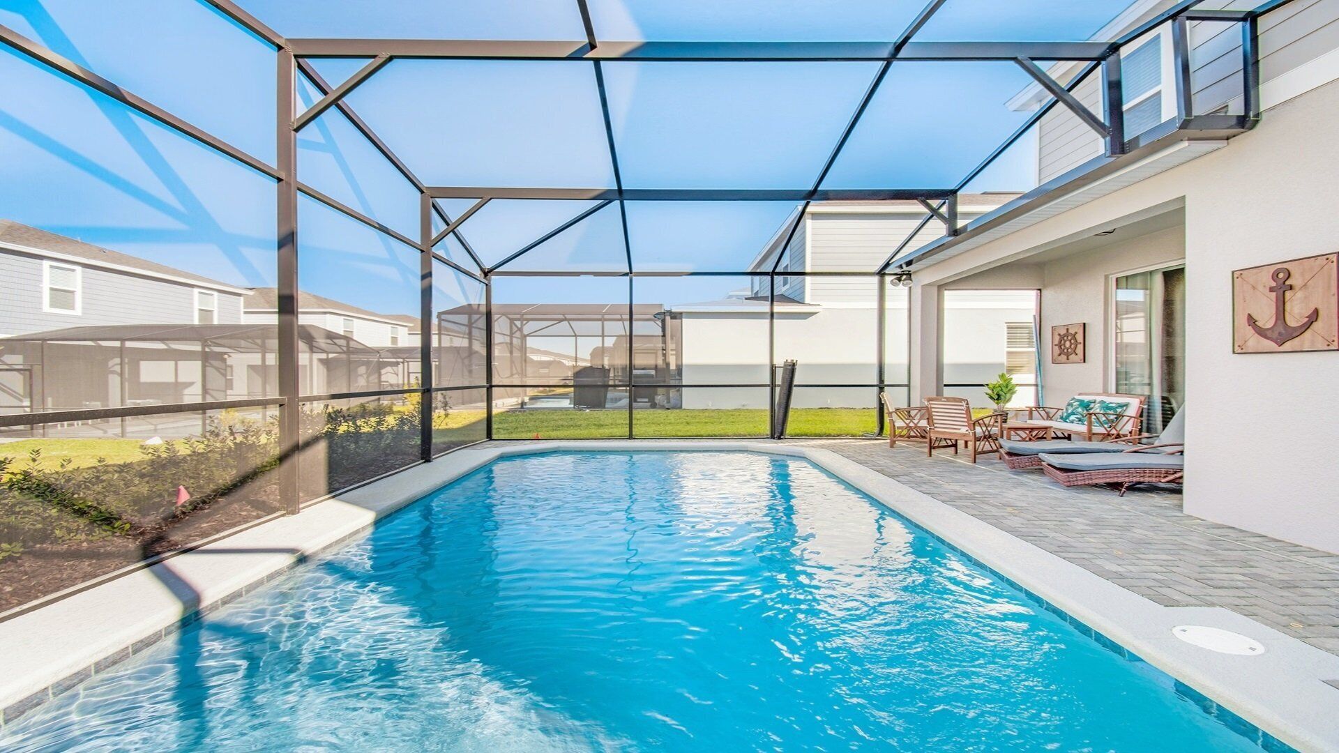 A swimming pool with a glass enclosure, outdoor seating, and a view of neighboring houses.