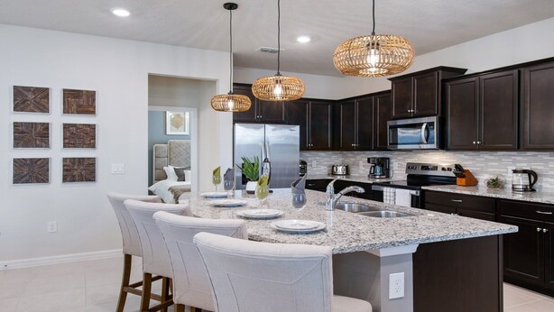 A modern kitchen with dark cabinets, a granite countertop, and a central island with bar stools. - Windsor Island 5br Villa W/private Pool Spa Disney (Davenport)
