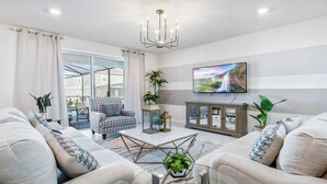A modern living room with a sofa set, a patterned armchair, a coffee table, and a TV mounted on the wall. - Windsor Island 5br Villa W/private Pool Spa Disney (Davenport)