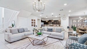 A spacious living room with a modern chandelier, a dining area with a chandelier, and a kitchen with dark cabinets and stainless steel appliances. - Windsor Island 5br Villa W/private Pool Spa Disney (Davenport)
