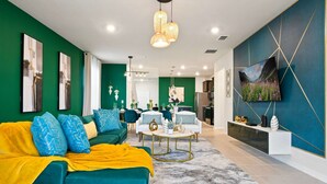 A modern living room with a teal sofa, yellow throw blanket, and a dining area with a white table and chairs. - Spacious Family Getaway at Windsor Island Resort (Davenport)
