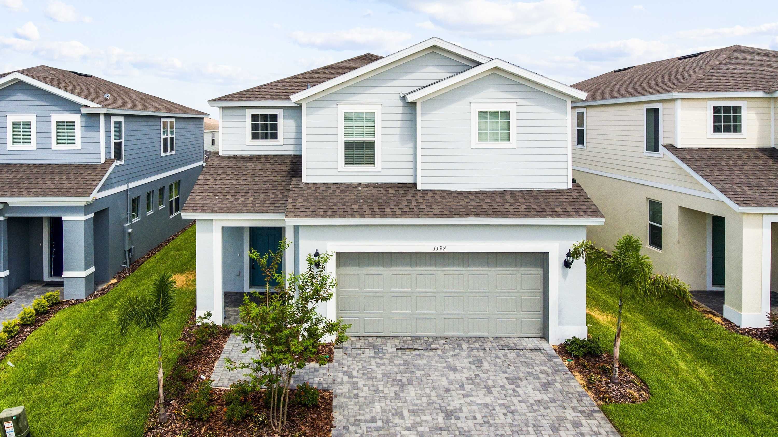 A modern two-story house with a garage, surrounded by well-maintained lawns and a brick driveway.