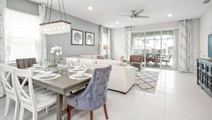 A modern living room with a dining area, a grey sofa, a chandelier, and a ceiling fan. - Windsor Island Luxe Villa w/ Pool/spa Near Disney (Davenport)