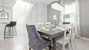 A dining area with a grey table set for four, white chairs, and a chandelier. - Windsor Island Luxe Villa w/ Pool/spa Near Disney (Davenport)