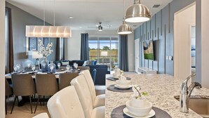 A modern hotel room with a dining area, a living room with a sofa and a TV, and a kitchen with a granite countertop and stainless steel sink. - Orlando Getaway: Near Disney, Pool, Resort (Davenport)