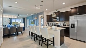 A modern kitchen with dark cabinets, stainless steel appliances, and a central island with bar stools. - Orlando Getaway: Near Disney, Pool, Resort (Davenport)