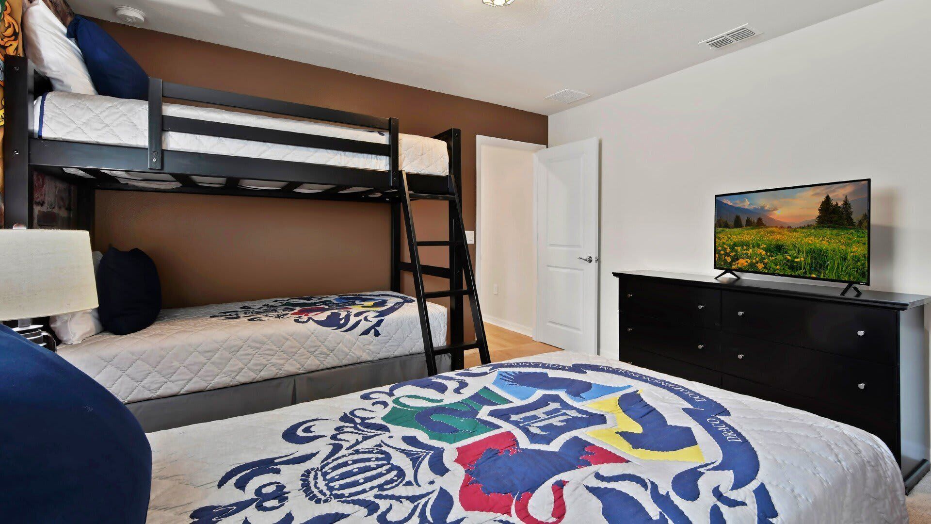 Une chambre avec des lits superposés, un bureau, une chaise, une télévision et une porte.