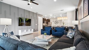 A modern living room with a sofa, two armchairs, a coffee table, and a TV. - Orlando Getaway: Near Disney, Pool, Resort (Davenport)