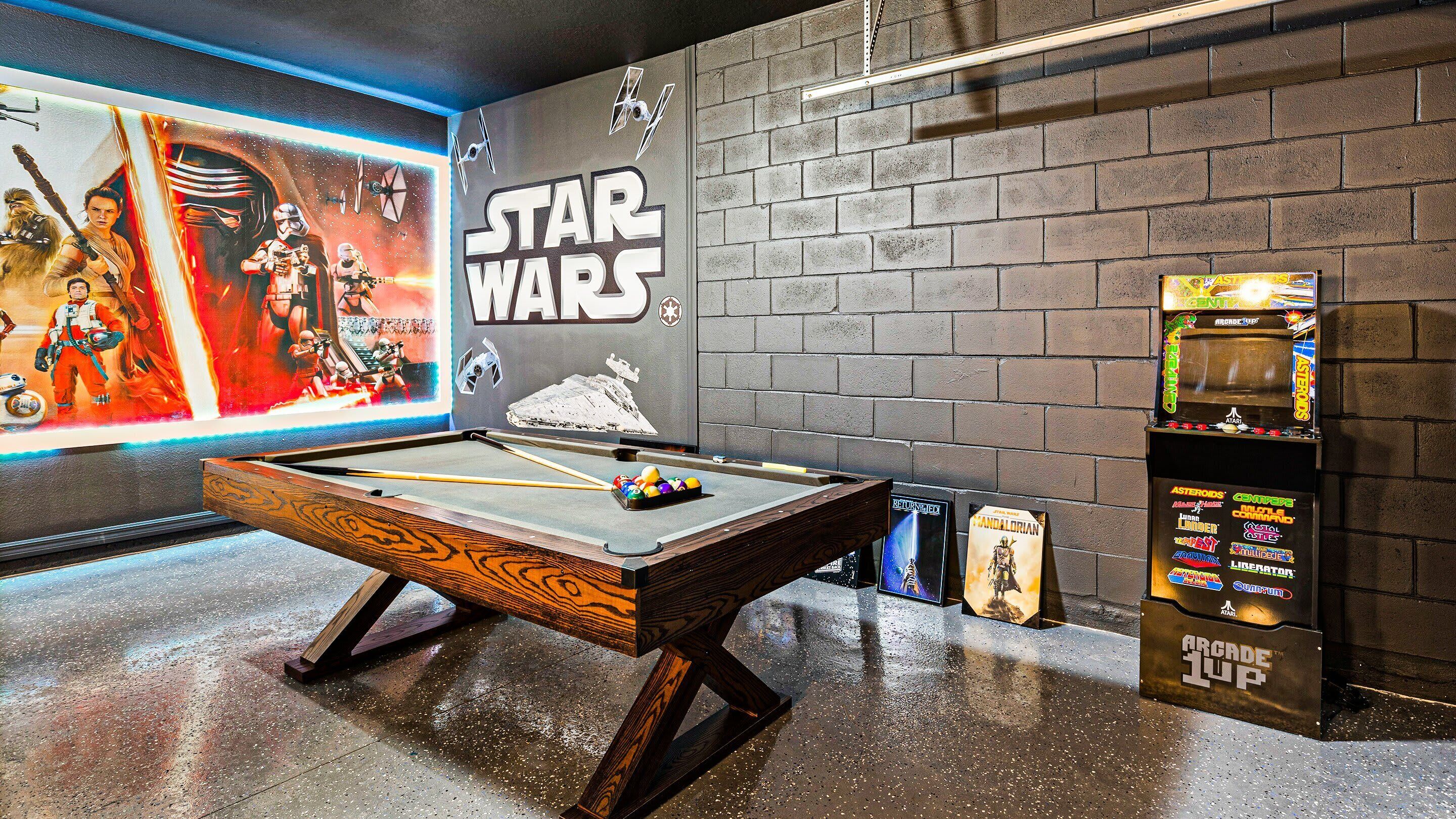 A pool table with Star Wars-themed decor, including a mural and a shelf with arcade games.