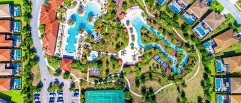 Luchtbeeld van een resort met meerdere zwembaden, tennisbanen en diverse gebouwen.