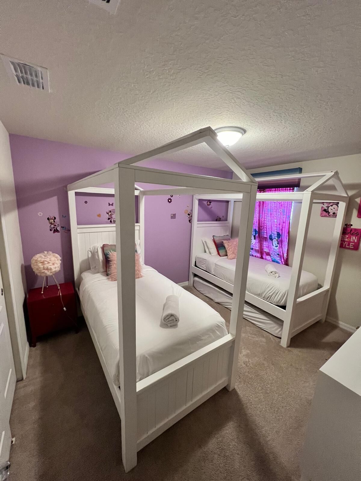 A bedroom with a four-poster bed, a red nightstand, and a window with curtains.