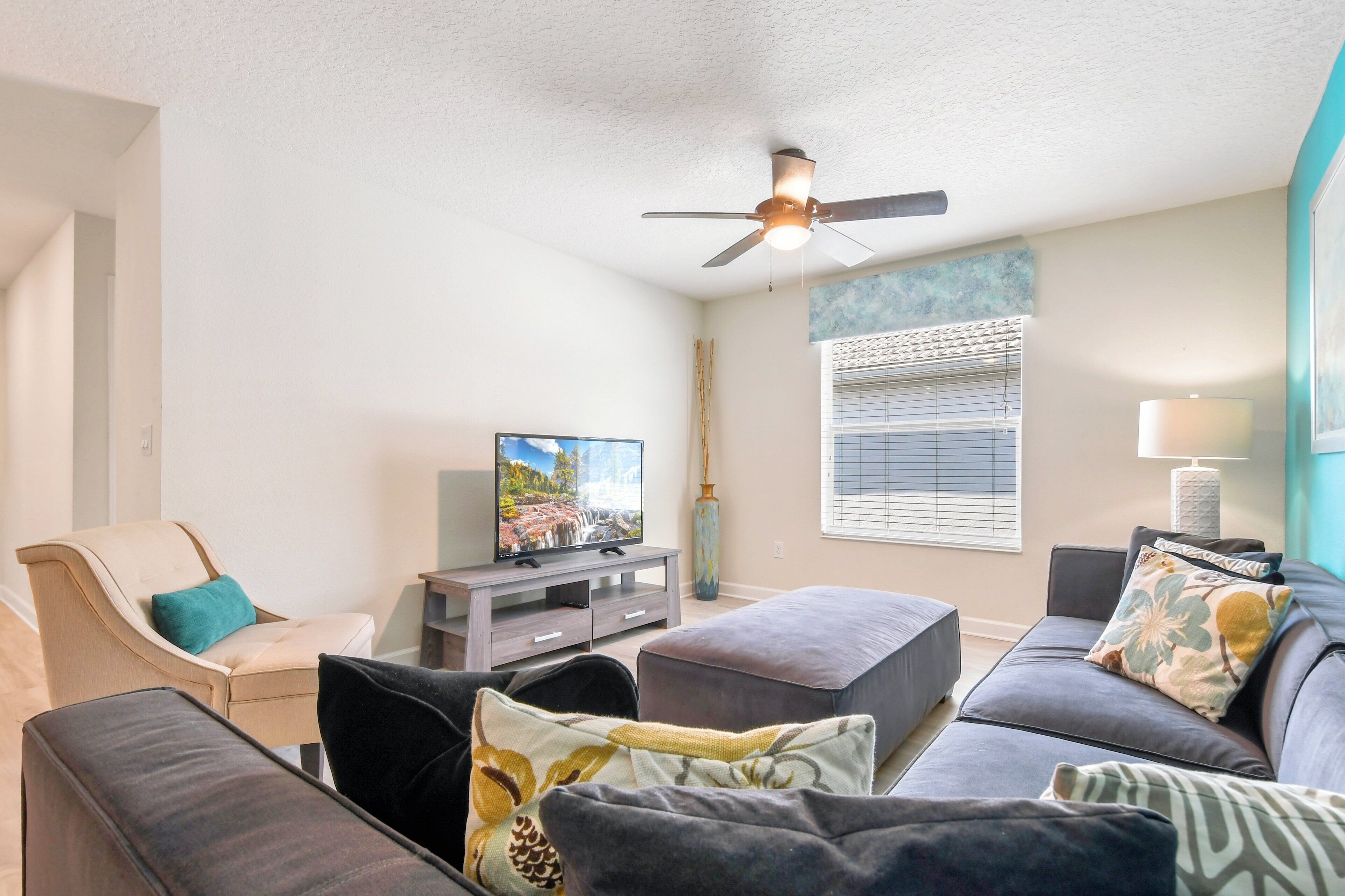 A living room with a TV, sofa, ottoman, and ceiling fan.