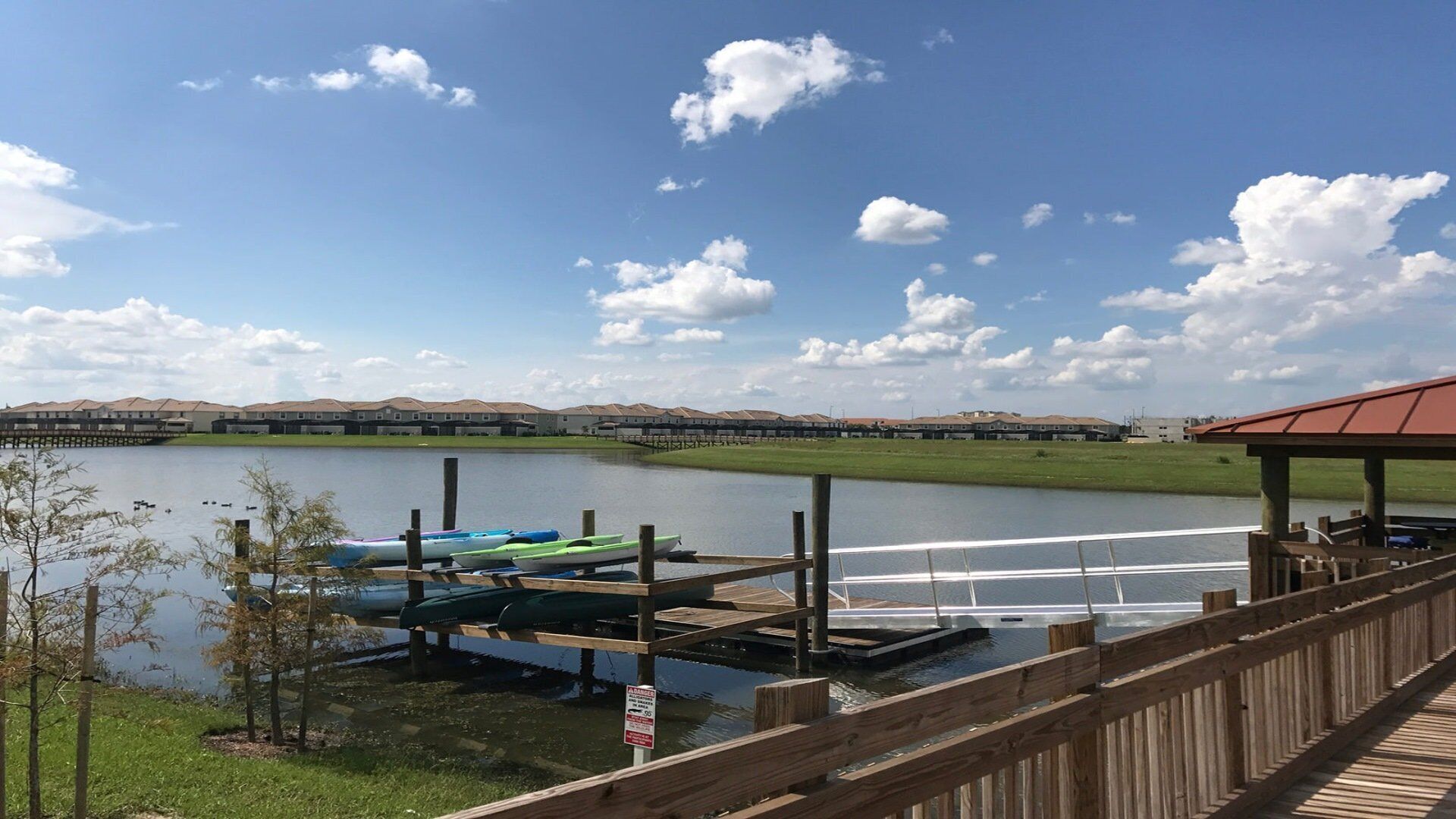 A lakeside view with a wooden dock, boats, and a row of buildings in the background.