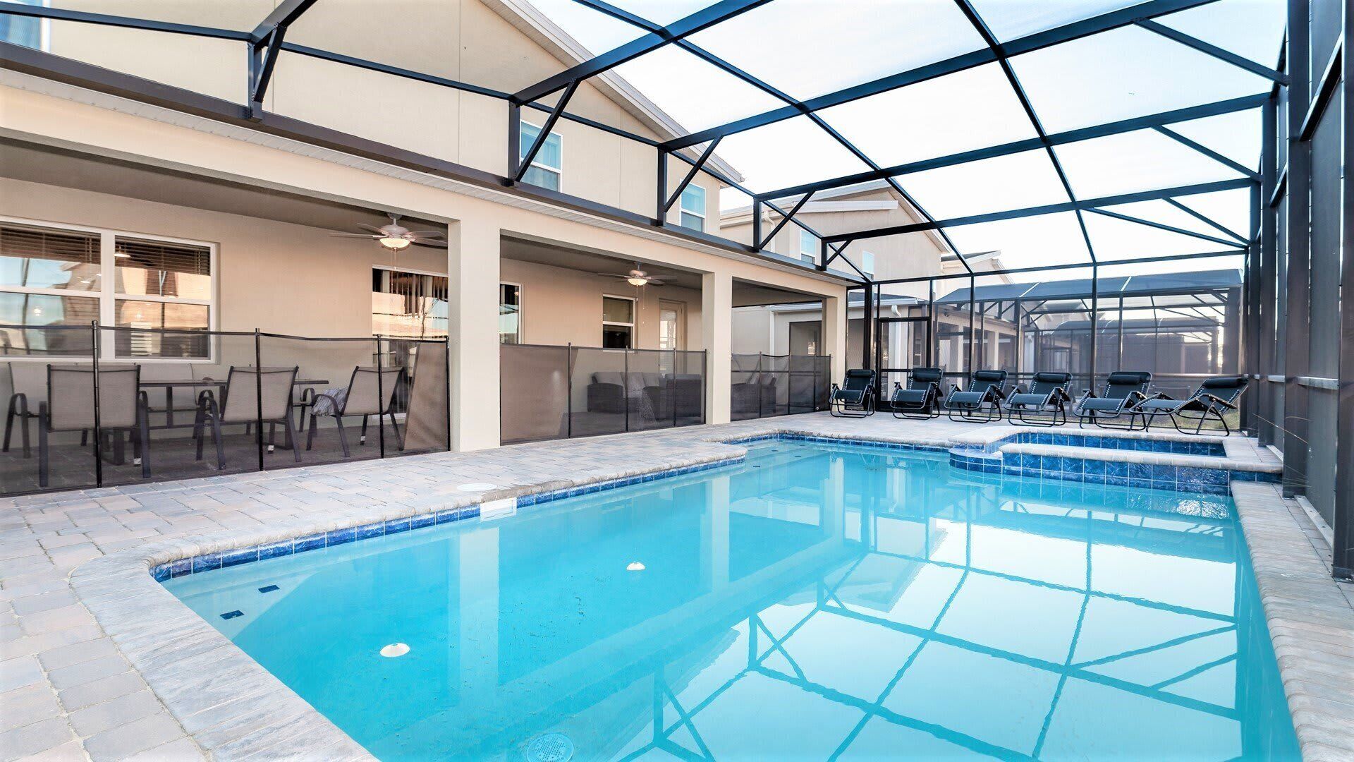 An indoor swimming pool with a glass ceiling, lounge chairs, and a bar area.