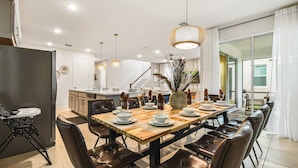 A modern dining area with a wooden table, leather chairs, and a central vase. - Solara Resort 6br Jurassic Pool Spa Villa Disney (Kissimmee)
