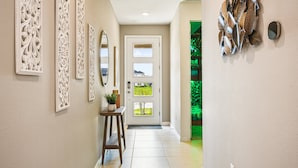A hallway with decorative wall panels, a potted plant, a bench, and a door with multiple windows. - Solara Resort 6br Jurassic Pool Spa Villa Disney (Kissimmee)