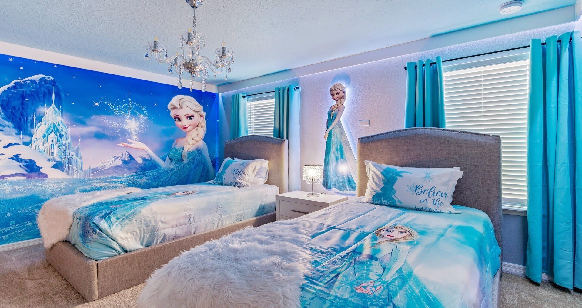 A bedroom with two beds, a chandelier, and a mural of a snowy landscape.