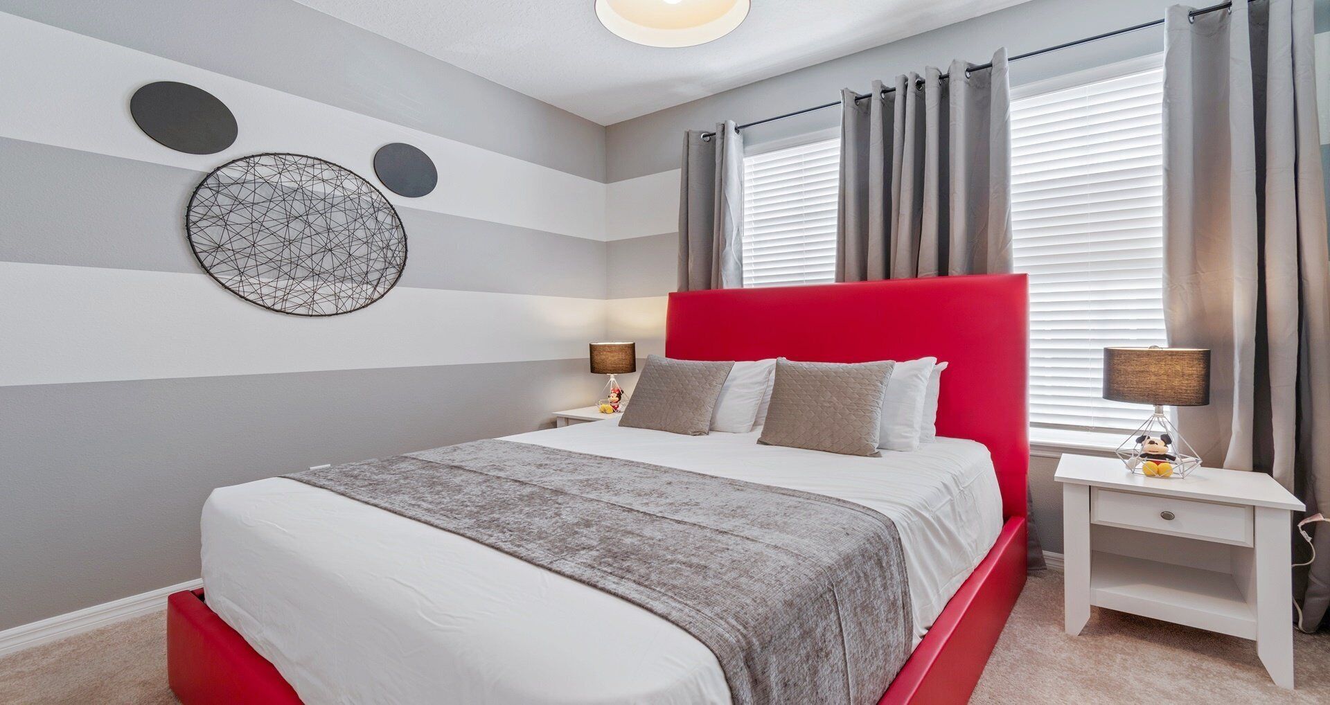 A modern bedroom with a red headboard, a grey and white striped wall, and a circular wall art piece.