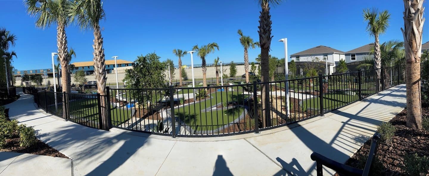 A fenced outdoor area with palm trees, a pool, and a clear blue sky.