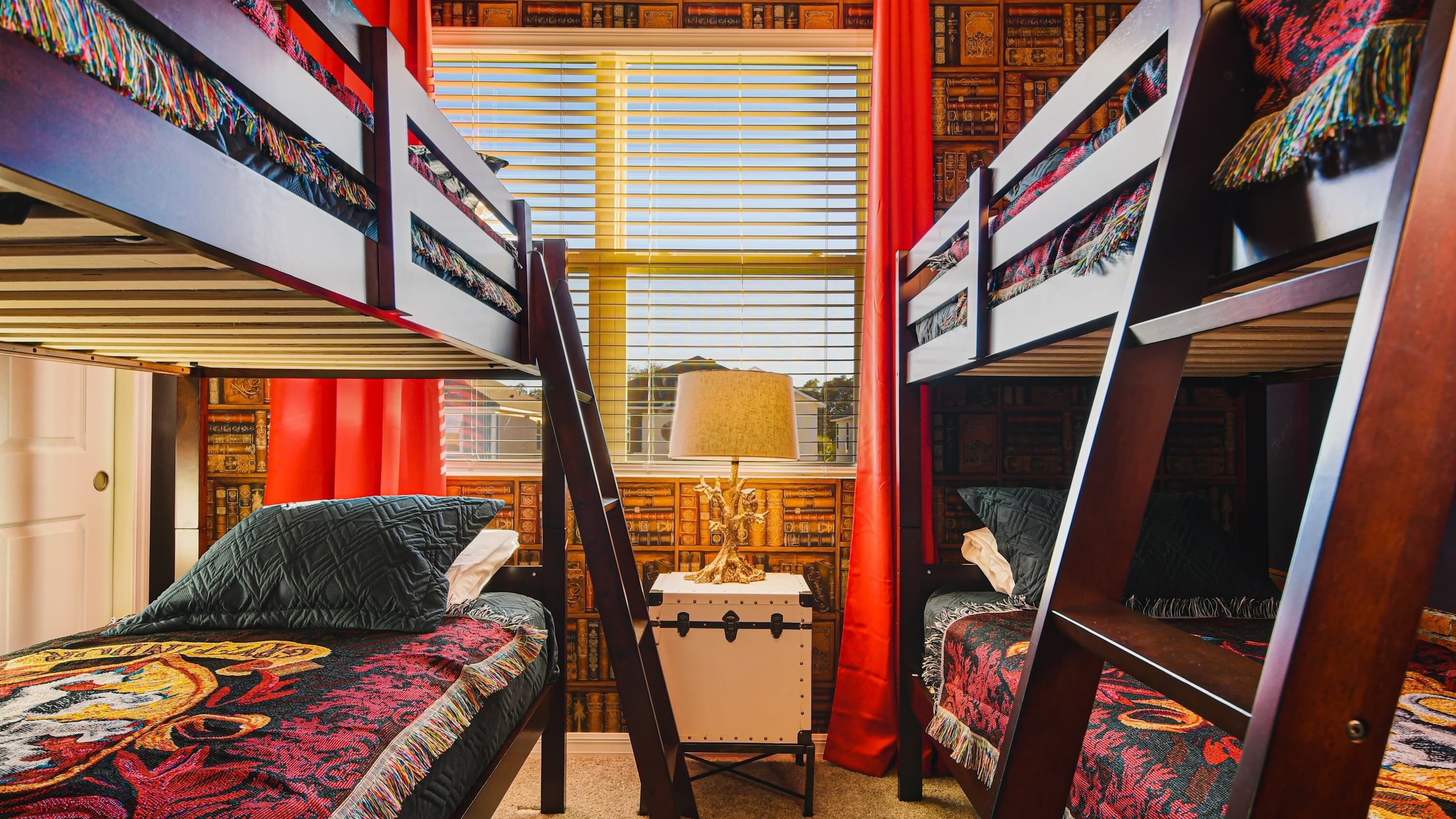 A room with bunk beds, a small table with a lamp, and a bookshelf filled with books.