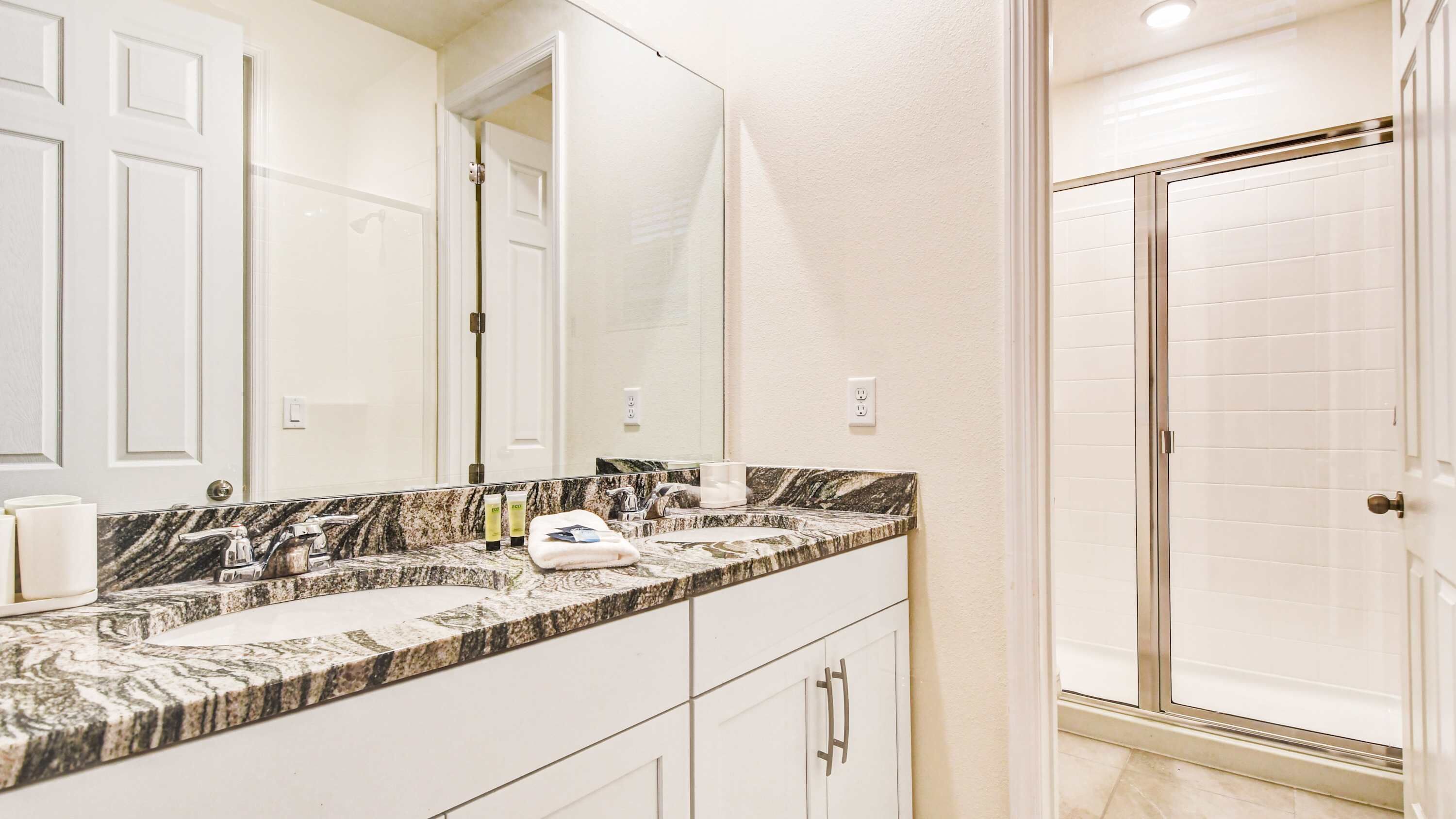 Une salle de bain avec un comptoir en marbre, un grand miroir, une douche et des meubles blancs.
