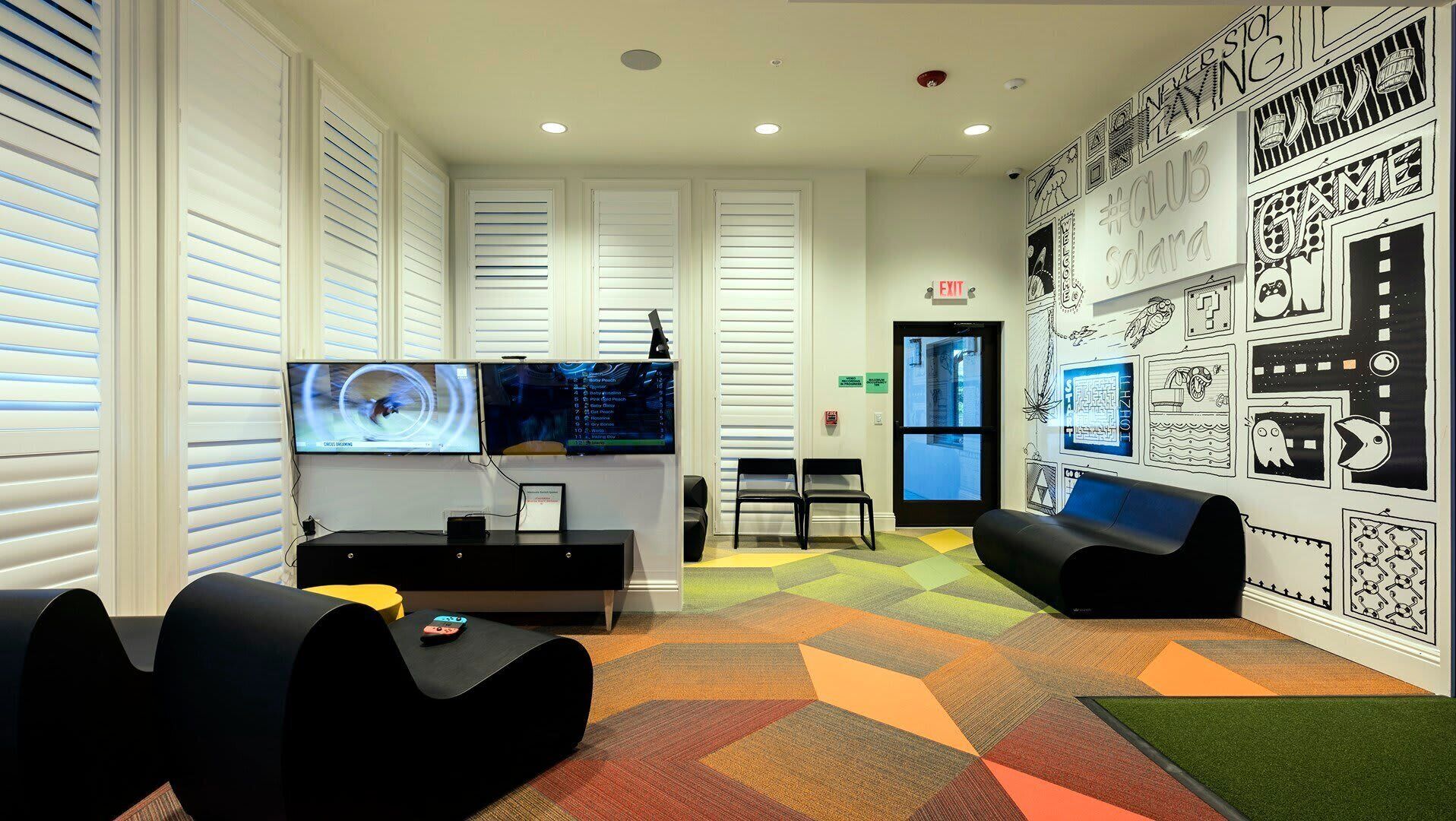 A modern lounge area with a flat-screen TV, comfortable seating, and a colorful geometric carpet.